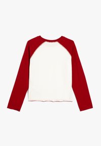 Langärmliges Shirt mit einem roten Raglan-Design. Der Körper ist weiß und verfügt über kontrastierende rote Ärmel sowie einen gewellten Saum. Aus weichem Baumwollmaterial.