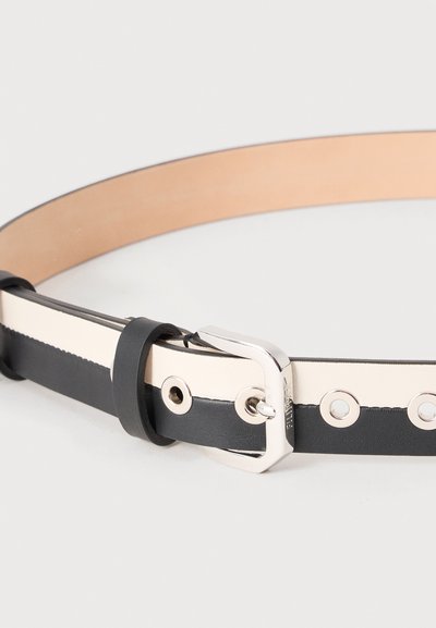 Δερμάτινη ζώνη με μαύρο και λευκό διαχωρισμό χρωμάτων, μεταλλική πόρπη και στρογγυλές μεταλλικές οπές σε ουδέτερο φόντο.