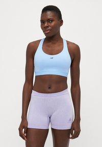 Sujeción deportiva de color azul claro con un logo en la parte delantera, combinado con unos pantalones cortos ajustados de color púrpura claro que presentan un pequeño detalle de marca. Textura de tela suave.