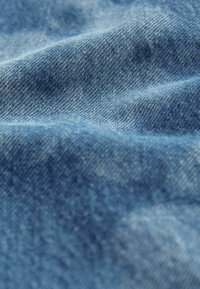 Close-up de tela vaquera, que presenta diferentes tonalidades de azul con un tejido texturizado y sutiles variaciones en el color y el patrón a lo largo.