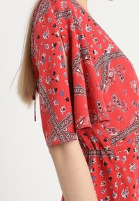 Rotes Kleid mit floralem Muster und kurzen Ärmeln, das Paisley- und geometrische Akzente aufweist, gefertigt aus leichtem Stoff.