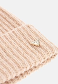 Berretto lavorato a maglia in beige chiaro con texture a coste. Dotato di un accento triangolare in metallo dorato. Progettato per calore e stile.