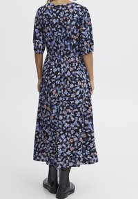 Květinové midi šaty s černým pozadím, zdobené modrými a růžovými květy, s nařaseným pasem a krátkými rukávy. Nositelná s černými kotníkovými botami.