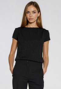 Czarna bluzka z krótkim rękawem z teksturowanej, błyszczącej tkaniny; okrągły dekolt; luźny krój; w zestawie z czarnymi spodniami.