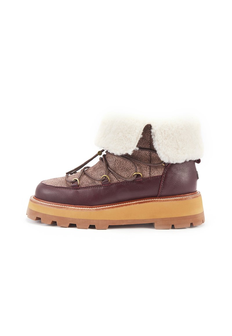Brązowy skórzany but z teksturowaną cholewą, białym futrzanym mankietem i grubą beżową podeszwą. Posiada metalowe oczka i dekoracyjne detale sznurowania.