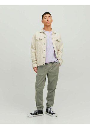 Giacca di jeans beige, t-shirt lavanda e pantaloni jogger verde chiaro. Sneakers alte nere con suola bianca. Outfit casual con design funzionale.