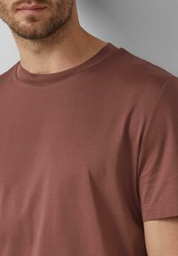 Hnedé tričko s krátkym rukávom a okrúhlym výstrihom, hladkou textúrou a minimálnymi švami, so štíhlym strihom bez vzorov alebo akcentov.