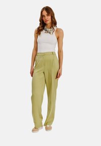 Svetle zelené kalhoty s vysokým pasem a volným střihem, zkombinované s bílým topem bez rukávů a vzorovaným šátkem kolem krku.