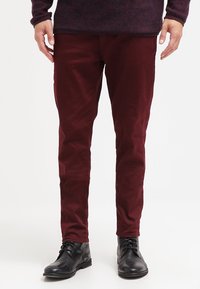 Pantaloni color bordeaux in cotone con design a taglio slim. Presentano tasche laterali e una texture liscia, abbinati a stivali neri con lacci.