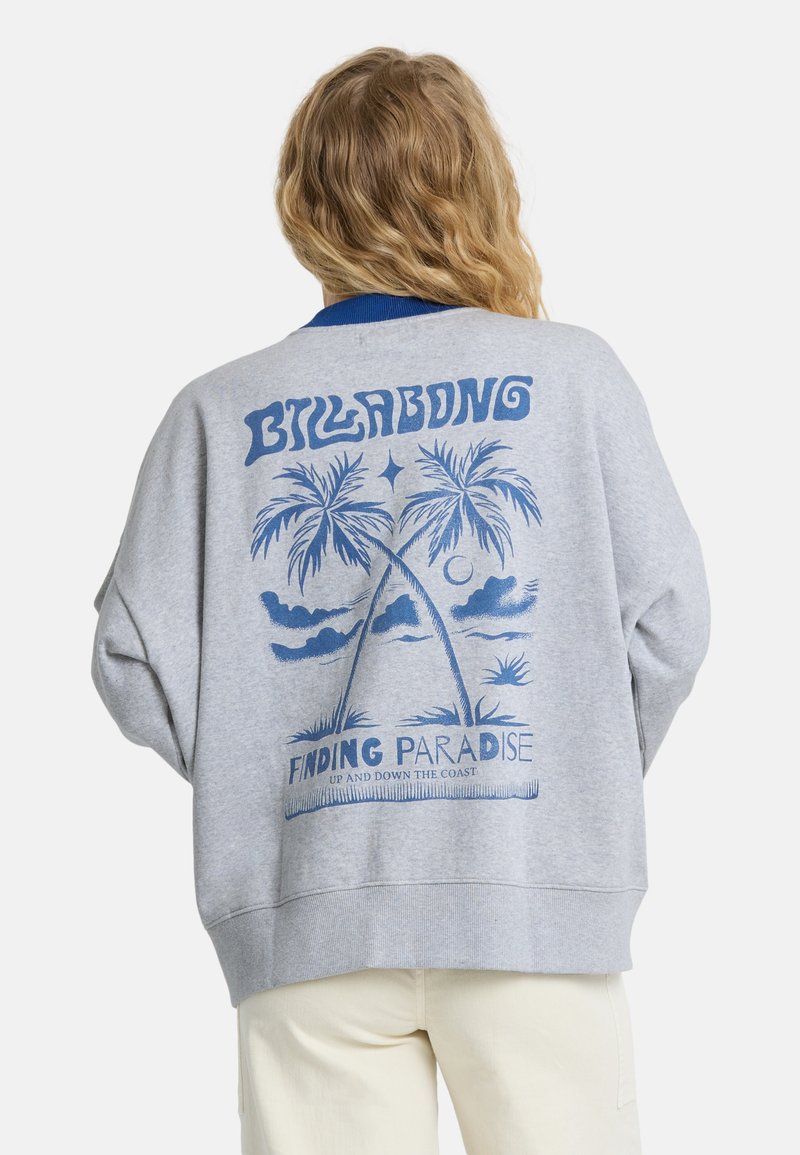 Person with long blonde hair wears gray sweatshirt with blue palm tree graphic and text "Billabong Finding Paradise" on the back.