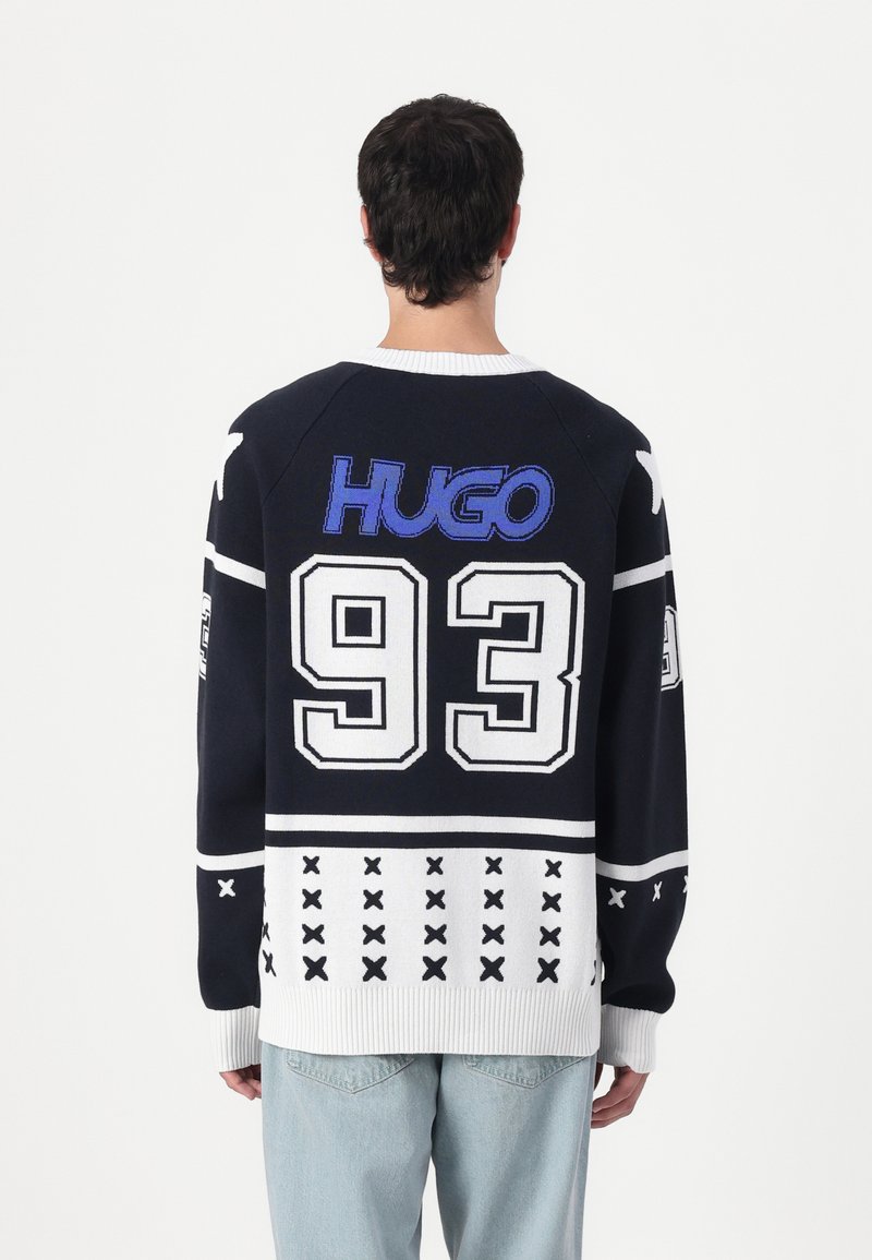 Marine strikkegenser med hvite og blå detaljer, stort "HUGO"-logo, nummer "93," og et geometrisk mønster i kanten.