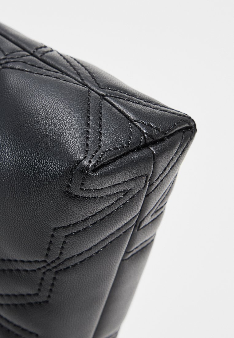 Angolo di una borsa in pelle nera con una texture trapuntata e dettagli di cuciture diagonali. Presenta una forma strutturata e angolare con una finitura liscia.