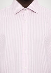 Camisa de rayas rosa claro hecha de tela con una textura suave, que presenta un cuello clásico y botones blancos. Pequeño logo en el pecho.