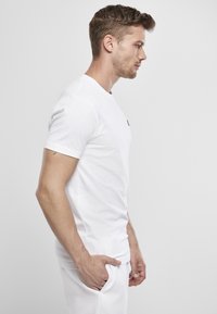 White cotton t-shirt with short sleeves and slim fit. Includes a small black logo on the left chest, plain design, and smooth texture.
