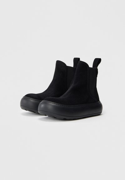 Schwarze Wildleder-Stiefeletten mit einer runden Gummisohle, elastischen seitlichen Einsätzen und Zuglaschen für ein einfaches An- und Ausziehen. Glatte Oberfläche und minimalistisches Design.