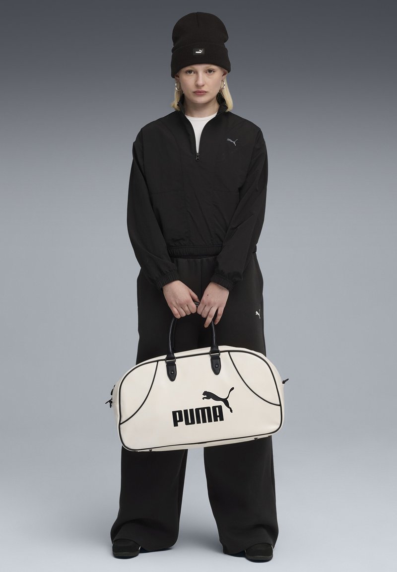 Musta vetoketjullinen takki ja housut, joissa on elastiset hihnat, yhdessä beigellä urheilukassilla, jossa on musta "PUMA" -logo ja tummat kahvat.