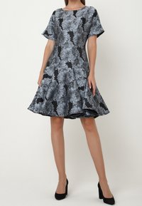 Květinové šaty v černé a šedé barvě s krátkými rukávy, rozšířenou sukni a kulatým výstřihem. Vyrobené z hladké tkaniny s texturovaným květinovým vzorem.