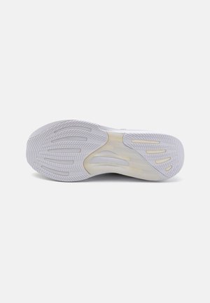 Semelle blanche de chaussure de sport avec motif de bande de roulement texturé et rainures flexibles sur un fond clair uni.
