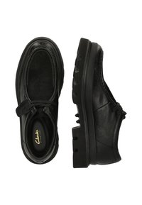 Zapatos de cuero negro con detalles texturizados, punta redonda y suela de goma negra con relieve pronunciado. Incluye un sistema de cordones y cierre de toggle.