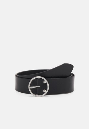 Ceinture en cuir noir enroulée avec une boucle ronde en métal argenté et une extrémité pointue sur un fond clair uni.