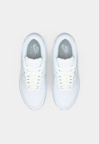 Białe sneakersy Nike z gładką skórzaną cholewką, okrągłym noskiem, płaskimi sznurowadłami i teksturowanymi szarymi wkładkami z logo marki.