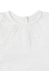 Weiße, strukturierte Bluse mit rundem Ausschnitt, die feine Falten und einen weichen, zerknitterten Stoff aufweist. Etikett sichtbar, das den Markennamen anzeigt.