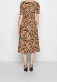 Brun mönstrad klänning med paisleymönster, korta ärmar och en utsvängd kjol, tillsammans med svarta högklackade sandaler.