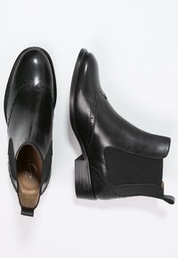 Černé kožené kotníkové boty mají elastické boční panely, strukturovaný vzor s perforacemi a nízký zvýšený podpatek.