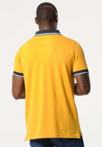 Geel polo shirt met navy kraag en accenten op de mouwen, korte mouwen en zijsplitsen. Zachte katoenmaterialen, eenvoudig ontwerp en gladde textuur.