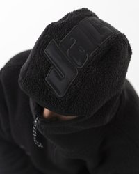 Balaclava in fleece nero con un esterno testurizzato e un pannello liscio con marchio. Presenta una cerniera al collo e un tessuto spesso e caldo.