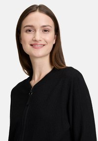 Zwarte zip-up jas van een textuurstof, met een geribde kraag en lange mouwen, voorzien van een soepele ritssluiting en zonder zichtbare patronen.