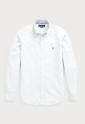 White long-sleeve button-up shirt made of cotton. Features a spread collar, button closure, and a small embroidered logo on the chest.