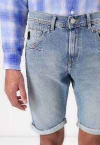Vaaleansiniset farkku shortsit, joissa on kulunut pinta. Ominaisuuksina käännetyt lahkeet, etu- ja takataskut sekä edessä nappikiinnitys.