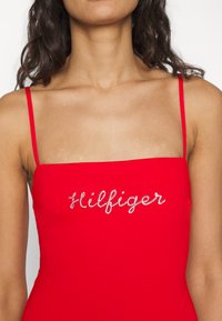 Abito rosso senza maniche con scollatura quadrata e logo "Hilfiger" ricamato in argento sul petto. Tessuto liscio, design aderente.