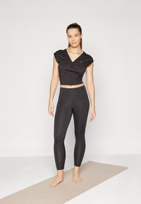 Black crop top with short sleeves and a twisted front design, paired with high-waisted black leggings, both made from a stretchy material.