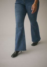 Niebieskie dzwony z denimu, z klasycznym krojem pięciu kieszeni. Połączone z czarnymi botkami na obcasie.