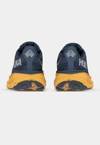 Rear view of blue running shoes with a textured finish, featuring a yellow midsole, HOKA branding, and gray rubber outsole details.