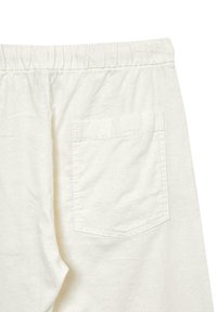 Cremefarbene Baumwollhose mit elastischem Bund und einer einzigen aufgesetzten Tasche auf der Rückseite. Glatte Textur mit minimalen Nähten.
