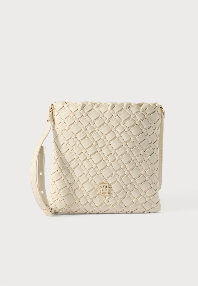 Austīta bēša ādas plecu soma ar plakanas formas dizainu, regulējamu siksnu un zelta krāsas logotipa akcentu priekšpusē.