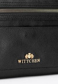 Černá kožená kabelka s texturovaným povrchem, zlatým zipem a zlatým emblémem se lvy a výrazně zobrazeným názvem "WITTCHEN".