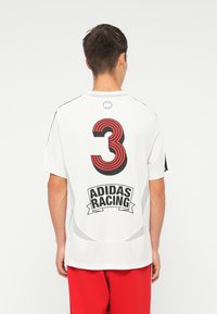 Bílé atletické tričko s velkým červeným a černým pruhovaným číslem "3" a textem "ADIDAS RACING" tučným černým písmem na zadní straně.