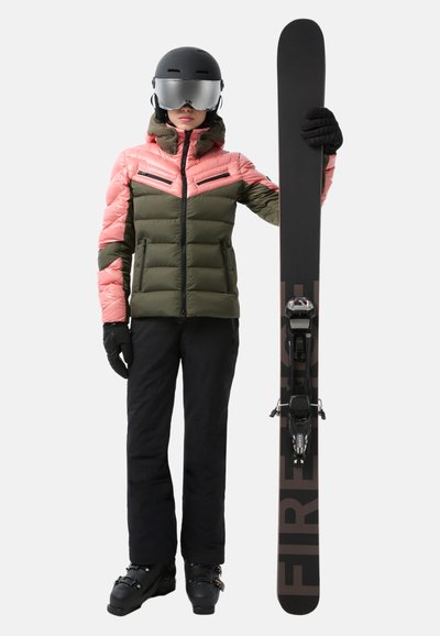 Skiausrüstung: pink-olivfarbene Daunenjacke mit Reißverschlüssen, schwarze Hose, schwarze Handschuhe und schwarze Skischuhe. Hält einen schwarzen Ski mit der Aufschrift "FIRE".