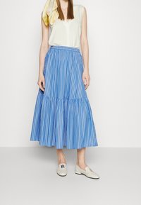 Jupe mi-longue rayée bleu et blanc avec une taille froncée et un bas évasé, associée à un haut léger et des chaussures blanches légères.