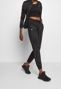 Czarny zestaw odzieży sportowej składający się z krótkiego topu na ramiączkach oraz kurtki zapinanej na zamek, z spodniami z elastycznym pasem. Teksturowana tkanina, minimalistyczny detal z białym logo.