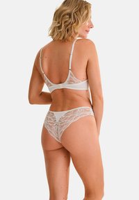 Witte kanten lingerie set met een semi-doorzichtig bralette en bijpassende string, voorzien van bloemmotieven en verstelbare bandjes.