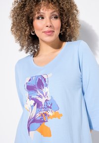 Maglia a manica lunga azzurro chiaro con un design grafico floreale in tonalità viola e arancione. Realizzata in morbido cotone, con scollatura a V.