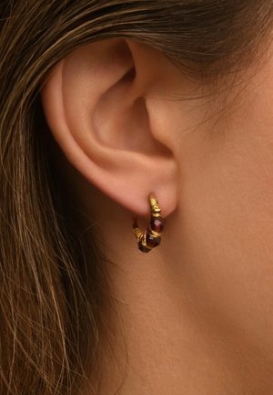 Boucles d'oreilles en or avec un design torsadé et deux perles de grenat rouge foncé. La texture est lisse avec une finition brillante.