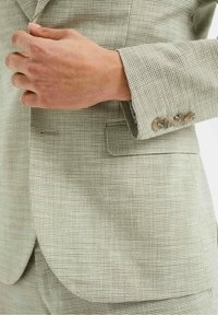 Ljust rutigt kavaj med en texturerad tyg, som har en spetsig revers, sidoficka och fyra-knäpps manschettdetalj.