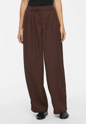 Pantalon marron à jambes larges avec plis sur l'avant, porté avec un haut noir et des chaussures noires, présenté de la taille aux pieds sur un fond uni.