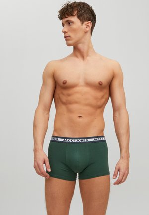 Grüne Baumwoll-Boxershorts mit einem weißen elastischen Bund, der das "JACK & JONES"-Logo trägt. Das Modell posiert vor einem neutralen grauen Hintergrund.